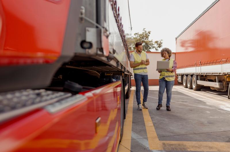 Two Professional Truck Drivers using Laptop while Talk and Perform a Technical Inspection of the Vehicle Before Next Drive. Professional Transportation Concept.