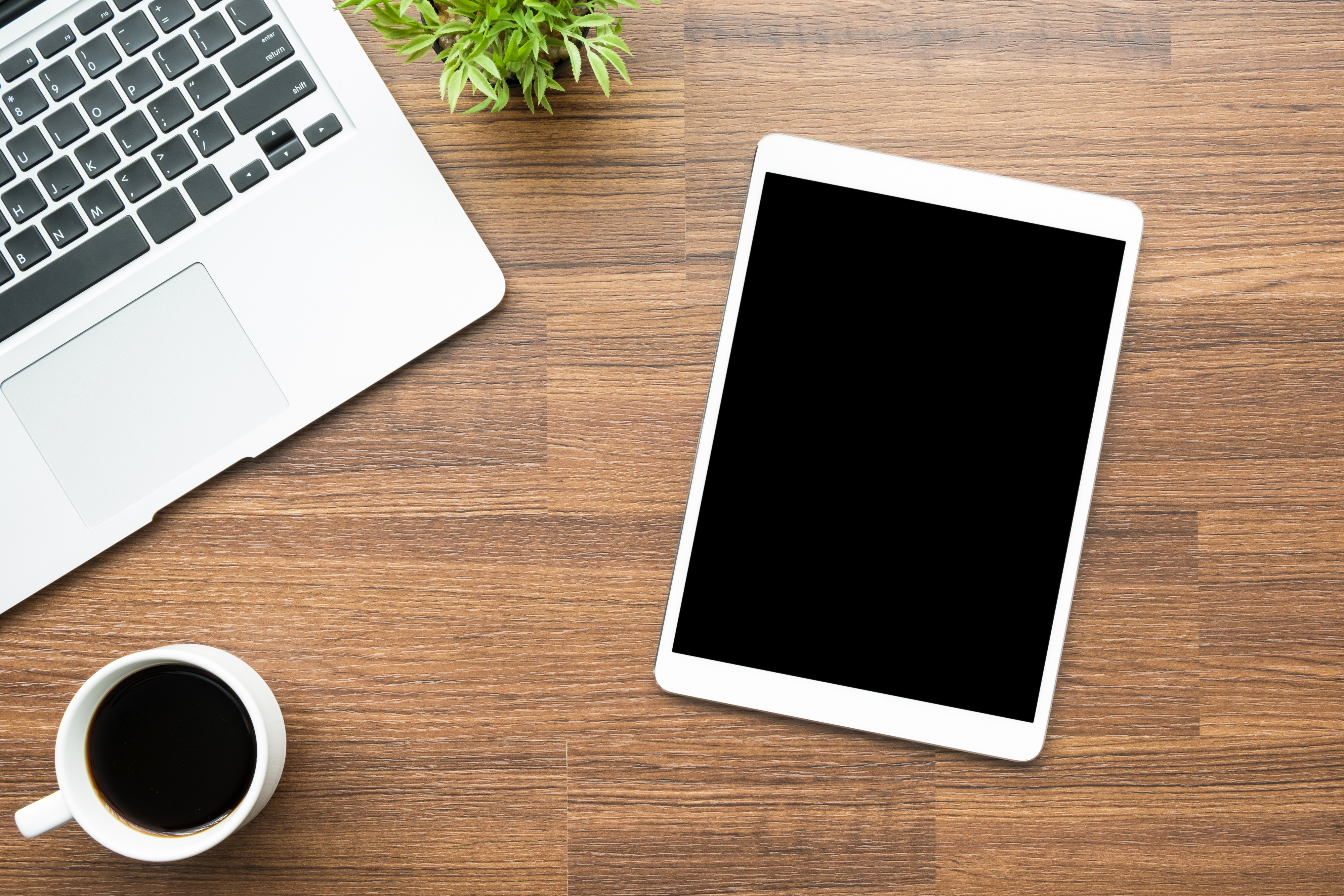 Wood office desk table with tablet with blank screen, laptop and cup of coffee. Top view, flat lay.