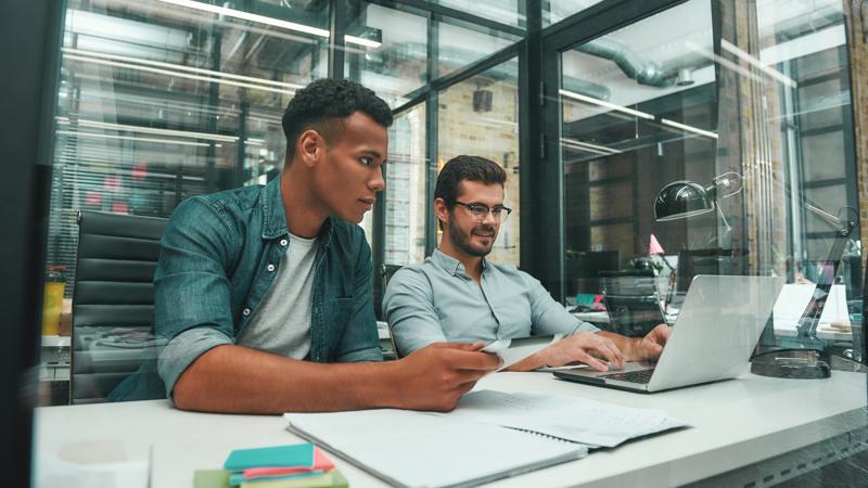 Working day. Two smart and handsome men looking at screen of laptop and discussing new project while working in modern office. Job concept. Workplace. Teamwork