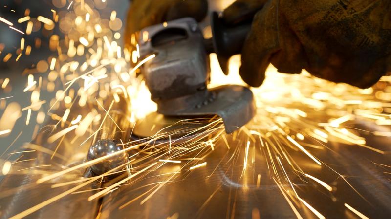 Grinding a metal door in production. Grinding a steel structure with an electric wheel at a factory. Door industry factory. Sparks from the grinding wheel.