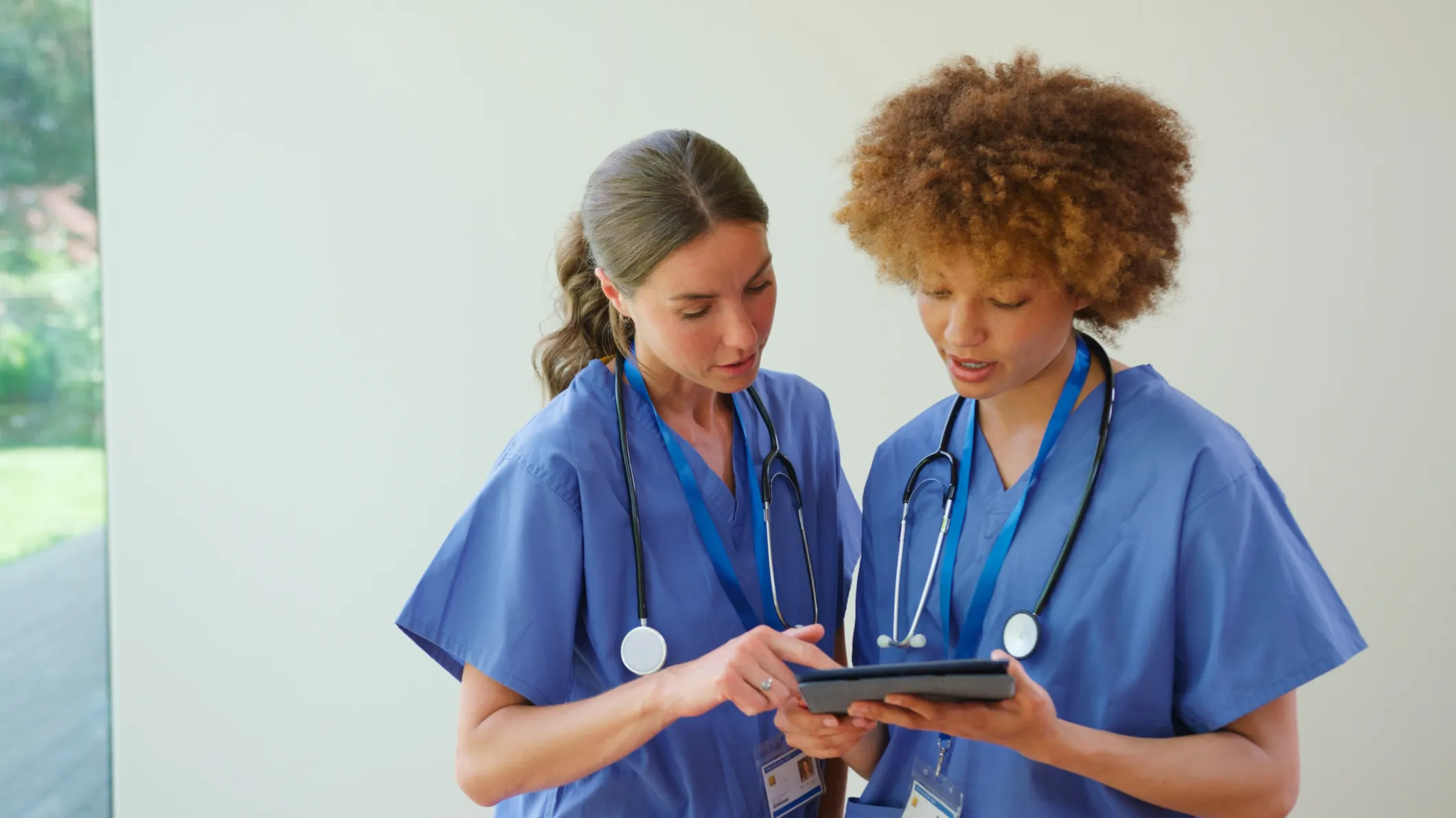 Two female doctors wearing scrubs looking at a tablet
