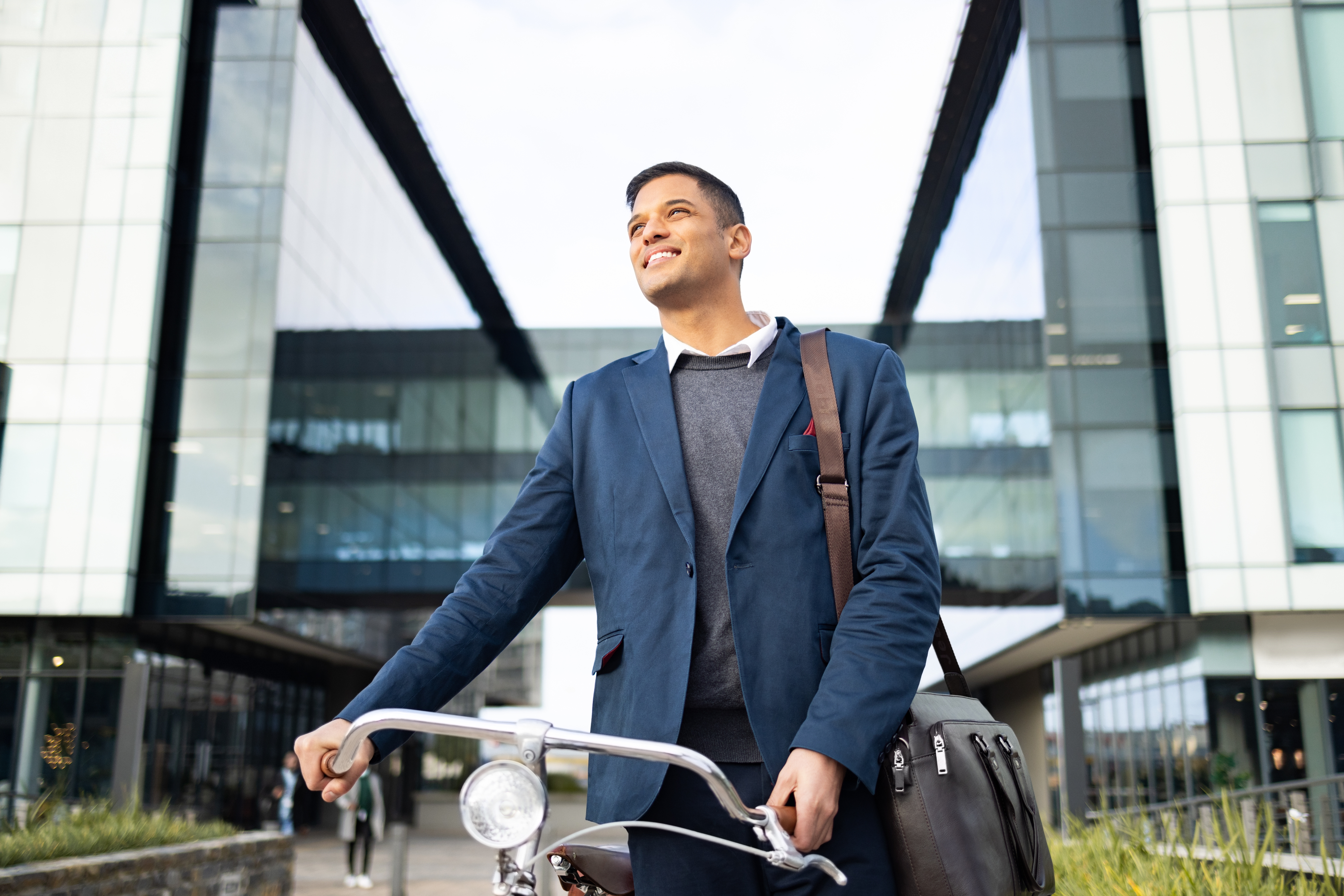 A man wearing business-casual attire is wheeling a bicycle outside an office building