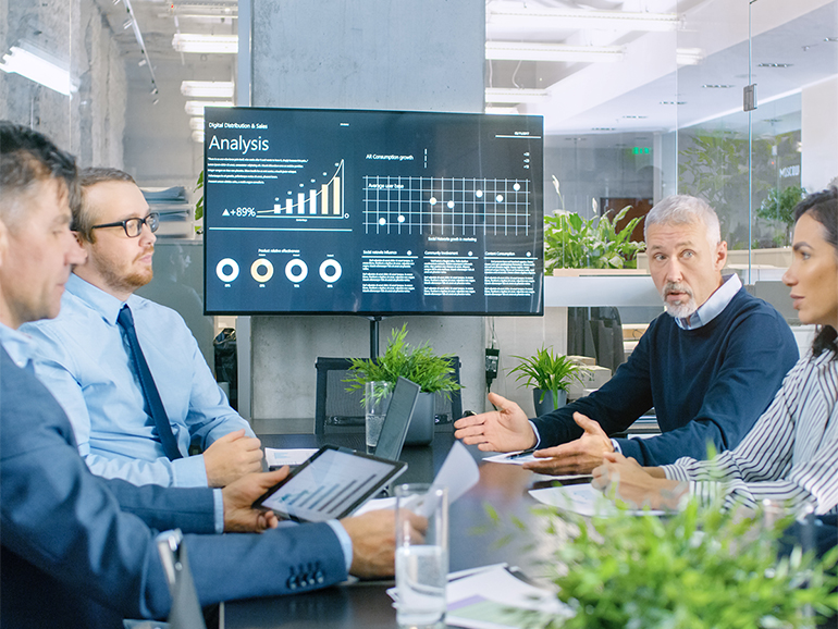 Colleagues having meeting in front of screen with data dashboard